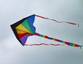 Multi coloured kite with a long tail and two streamers sours high in the sky