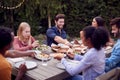 Multi-Cultural Friends At Home Sitting At Table Enjoying Food At Summer Garden Party