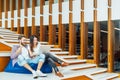 Multi-ethnic college student couple celebrate together with laptop on stairs in university campus or modern office