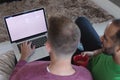 Multi ethnic gay male couple sitting on couch using laptop with copy space on screen at home Royalty Free Stock Photo