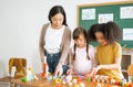 Multi-ethnic group of children school standing and playing with colorful blocks on table with Female Asian teacher in classroom. Royalty Free Stock Photo