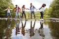 Multi ethnic group of five adult friends hold hands and help each other while carefully crossing a stream standing on stones durin Royalty Free Stock Photo