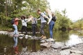 Multi ethnic group of five young adult friends hold hands balancing on rocks to cross a stream during a hike Royalty Free Stock Photo