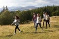 A multi ethnic group of five young adult friends smile while walking on a rural path during a mountain hike, side view