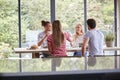 Multi ethnic group of four young adult friends celebrating at a dinner party raising their wine glasses, seen from kitchen island