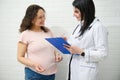 Female doctor gynecologist with clipboard consulting a gravid pregnant woman, prescribing medicines. Pregnancy. 9 month Royalty Free Stock Photo