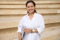 Multi ethnic pretty woman holding laptop, smiling looking at camera, standing against beige marble city steps backdrop Royalty Free Stock Photo