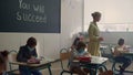 Multi ethnic students in face masks doing test in classroom with teacher