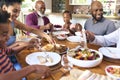 Multi-Generation Family Sitting Around Table Serving Food For Meal At Home Together