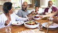 Multi-Generation Family Sitting Around Table Serving Food For Meal At Home Together