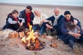 Multi Generation Family Sitting By Fire On Winter Beach