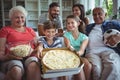 Multi-generation family sitting with popcorn and pizza while watching soccer match Royalty Free Stock Photo