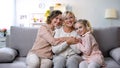 Multi-generation females hugging on home sofa smiling camera, family closeness