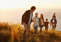 Follow the leader. A multi-generational family walking up a grassy hill together at sunset with the ocean in the Royalty Free Stock Photo