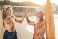 Multi generational surfer friends hands five on the beach after surf session - Focus on senior man face