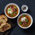 Multi grain and vegetables soup with grilled cheese sandwiches and crispy bacon on a dark background, top view. Delicious comfort