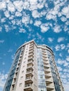 A multi-storey circular building with blue windows against a background of blue sky and white clouds. Royalty Free Stock Photo