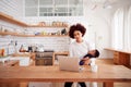 Multi-Tasking Mother Holds Sleeping Baby Son And Works On Laptop Computer In Kitchen Royalty Free Stock Photo