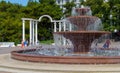 Multi-tiered musical Singing fountain fountain against white arch. Pool and bowls of fountain are made of red granite. Royalty Free Stock Photo