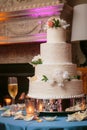 Multi tiered wedding cake with white flowers and cream frosting on a table with candles and champagne glasses - wedding cake