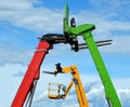 Multicolor booms of forklifts and aerial platform against blue sky with clouds