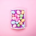 Multicolor eggs in a white tray. Creative Easter concept. Modern solid pink background.