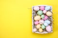 Multicolor eggs in a white tray. Creative Easter concept. Modern solid yellow background.