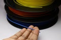 Multicolor filament spools or reels laid flat with hands holding blue filament