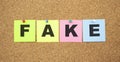 Multicolor notes with letters pinned on a cork board. Word FAKE Royalty Free Stock Photo