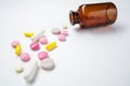 Multicolor pills and tablets spilling out from glass pill bottle on white.