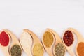Multicolored asian spices in quaint spoons on white wooden background.