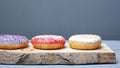 Multicolored assorted red,white,violet donuts coated with glaze and sprinkled with Easter powder on wooden stand gray backgroundn