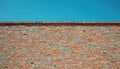 Multicolored brick wall texture with varied tones of orange, brown, blue bricks. Clear blue sky forms backdrop above weathered Royalty Free Stock Photo