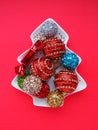 Multicolored Christmas balls on a white plate in the form of a Christmas tree. Christmas tree. Red background or crimson