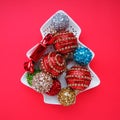 Multicolored Christmas balls on a white plate in the form of a Christmas tree. Christmas tree. Red background or crimson