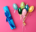 Multicolored decorative Easter eggs decorated with sequins and blue paper scroll on a pink background Royalty Free Stock Photo