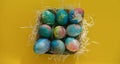 Multicolored Easter eggs lie in a basket on a yellow background, with bright colored sweets, close-up. Concept Easter and holiday Royalty Free Stock Photo