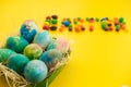 Multicolored Easter eggs lie in a basket on a yellow background, with bright colored sweets, close-up. Concept Easter and holiday Royalty Free Stock Photo