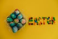 Multicolored Easter eggs lie in a basket on a yellow background, with bright colored sweets, close-up. Concept Easter and holiday Royalty Free Stock Photo