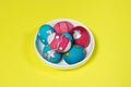 Multicolored Easter eggs in a white plate on a yellow background. Patterns and designs on colored dyed eggs Royalty Free Stock Photo