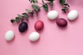 Multicolored easter painted eggs in pink and white tones with a green eucalyptus branch on a pink background