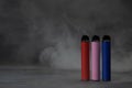 multicolored electronic cigarettes vape on dark background with smoke. Royalty Free Stock Photo