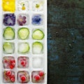 Multicolored frozen ice cubes with fruits, flowers and vegetables on a dark background