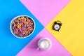 Multicolored fruit loops, jug of milk and alarm clock against the geometric background Royalty Free Stock Photo