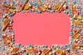 Multicolored glazed dragees and other sweets are arranged in the form of a frame on a coral background. Royalty Free Stock Photo