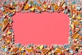 Multicolored glazed dragees and other sweets are arranged in the form of a frame on a coral background. Royalty Free Stock Photo