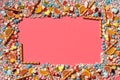 Multicolored glazed dragees and other sweets are arranged in the form of a frame on a coral background. Royalty Free Stock Photo