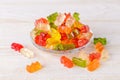 Multicolored gummy bears candy on a glass plate over white wood table. Jelly sweets of differenr colors. Popular gummies made from