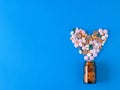Multicolored heart-shaped pills pour out of a glass brown bubble on a blue background