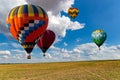 Multicolored hot air balloons fly in blue sky with white clouds over green field Royalty Free Stock Photo